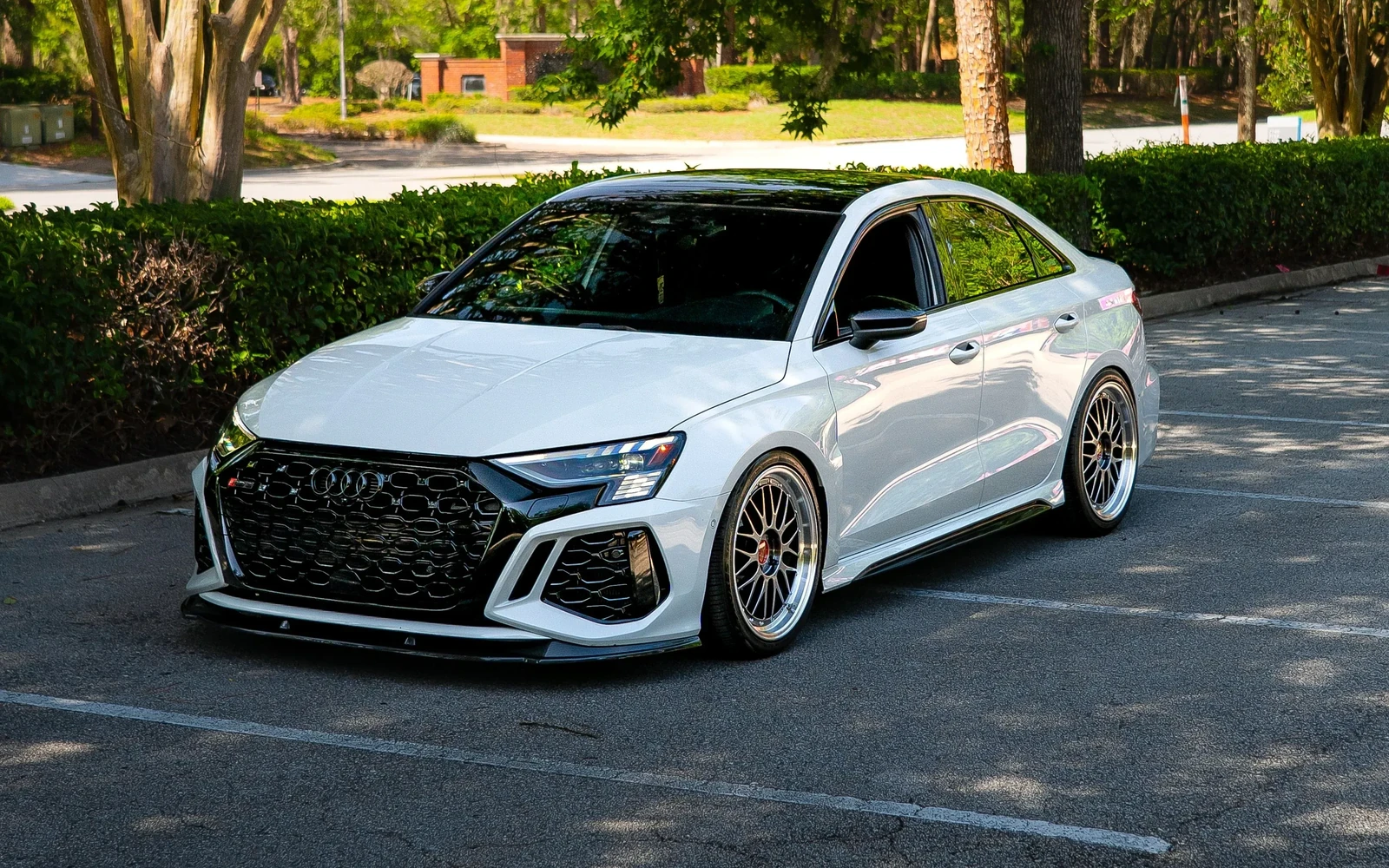 White Audi sedan parked beneath trees with dark rear windows.