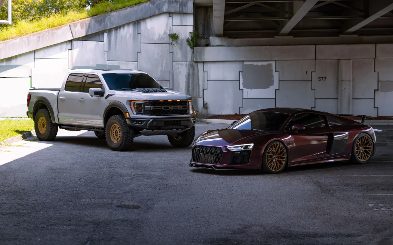 Audi R8 and Ford pickup with dark windows parked beneath a concrete overpass.