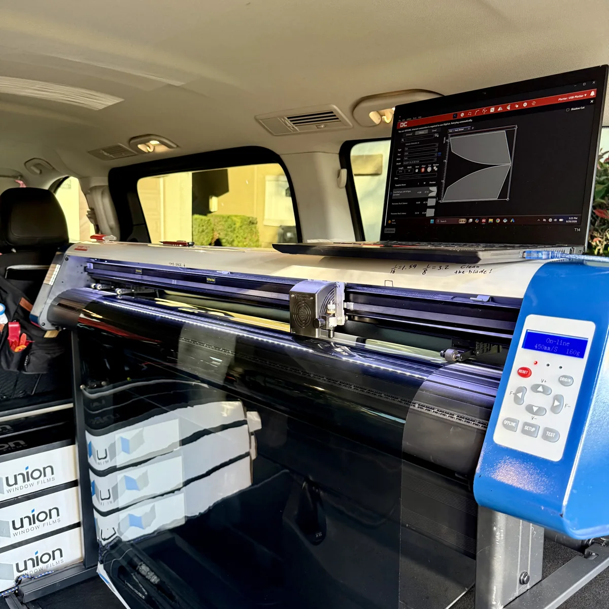 Window tint cutting plotter with film loaded and digital window patterns displayed on a laptop in the mobile installation vehicle
