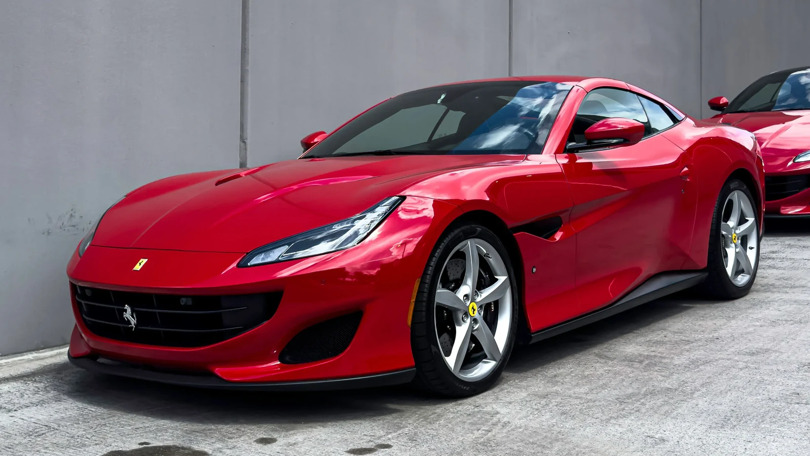 Red Ferrari parked beside a concrete wall, showing its windshield and side glass.
