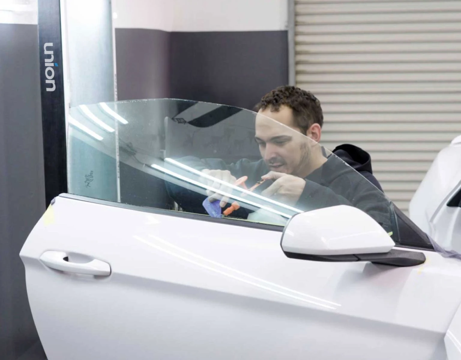 Installer fitting window film to the front door glass of a white car.