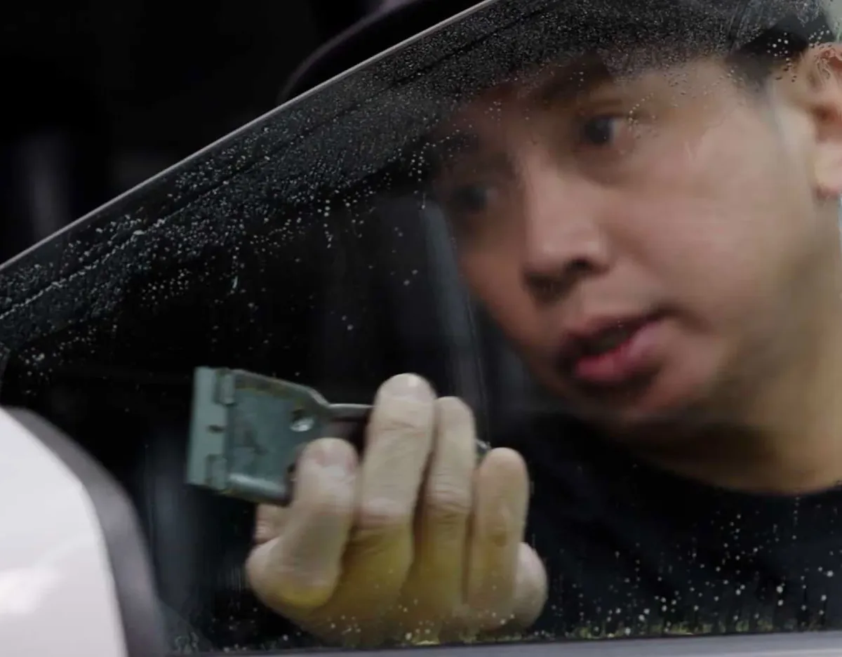 Installer using a scraper to prepare wet car window glass.