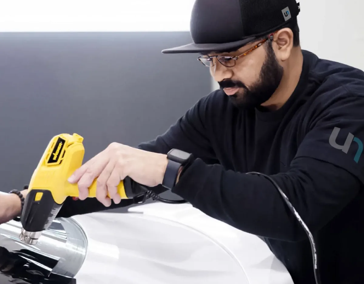 Installer using a heat gun to shape window film on curved glass.