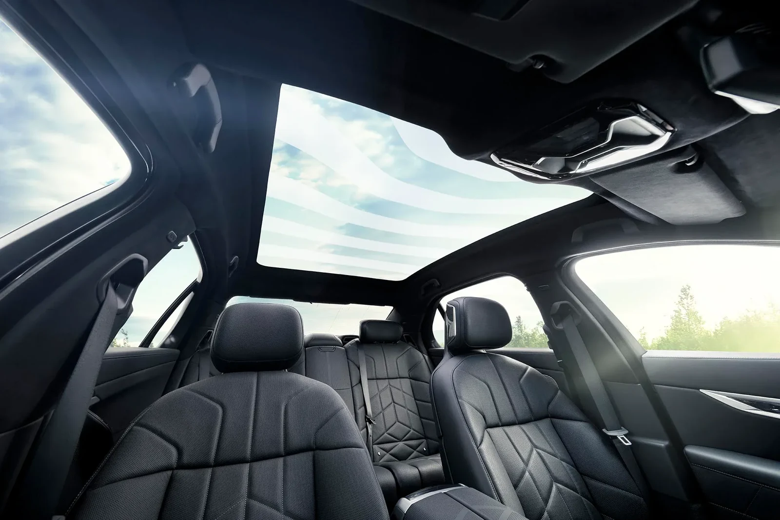 Vehicle interior with a broad panoramic glass roof above the front and rear seats.