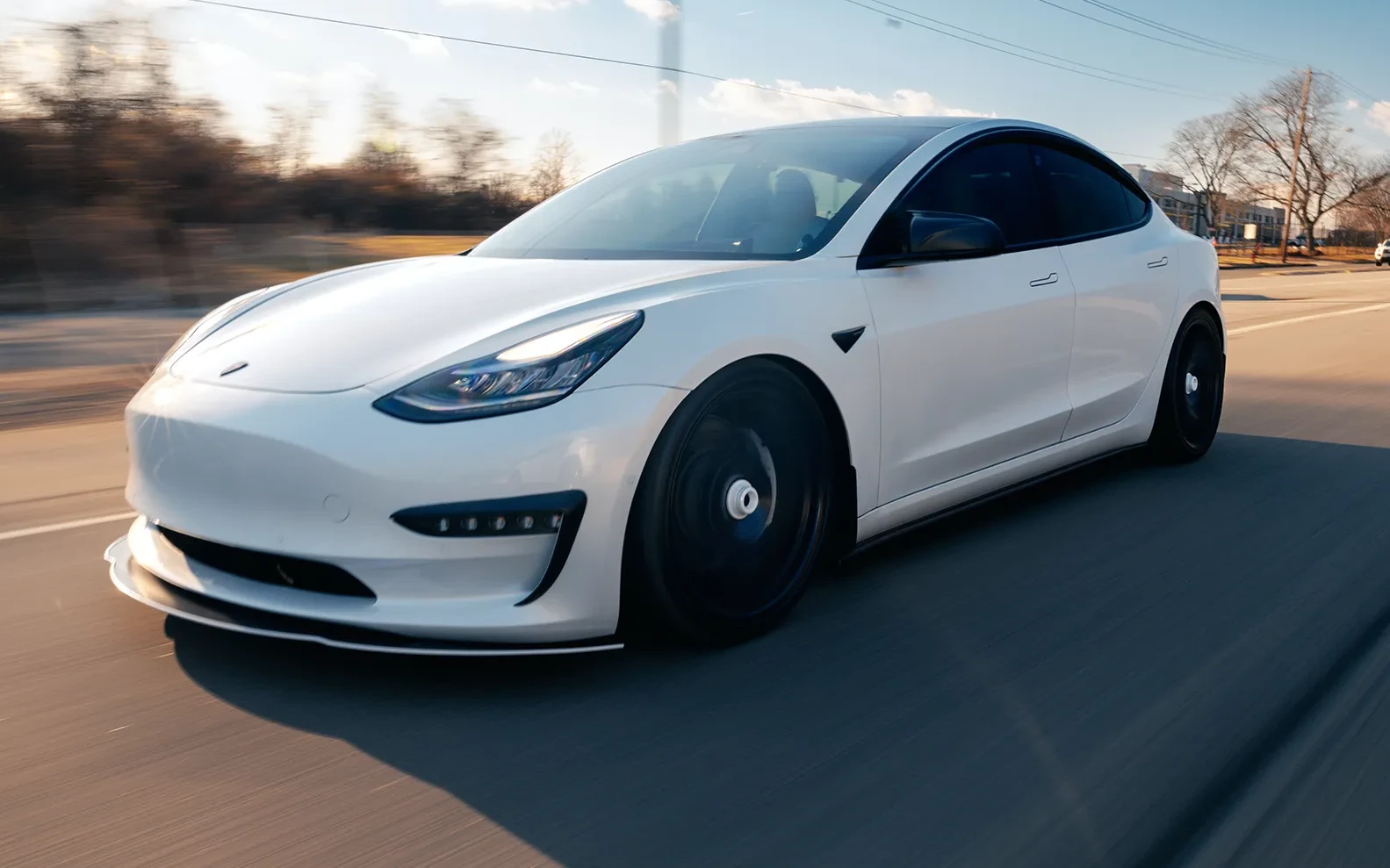 White Tesla Model 3 with dark side windows on a sunlit road.