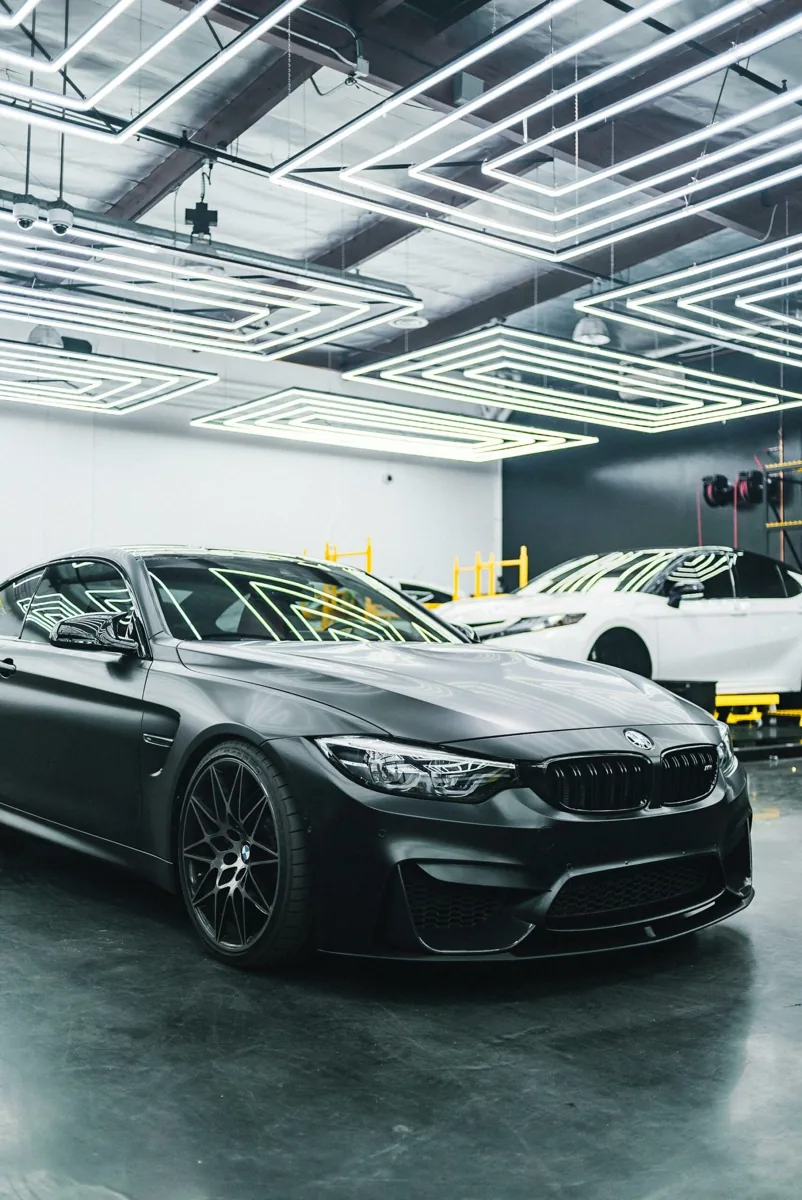 Gray BMW and white SUV with dark side windows in a workshop.