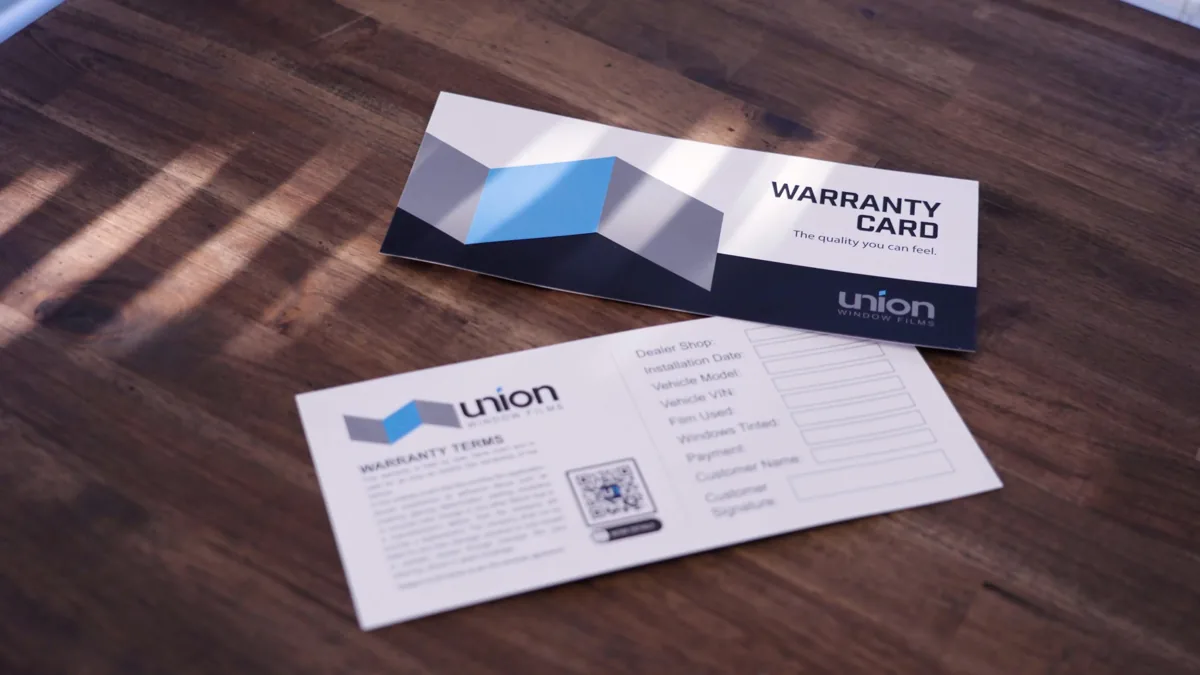 UNION Window Films warranty cards on a wooden table.